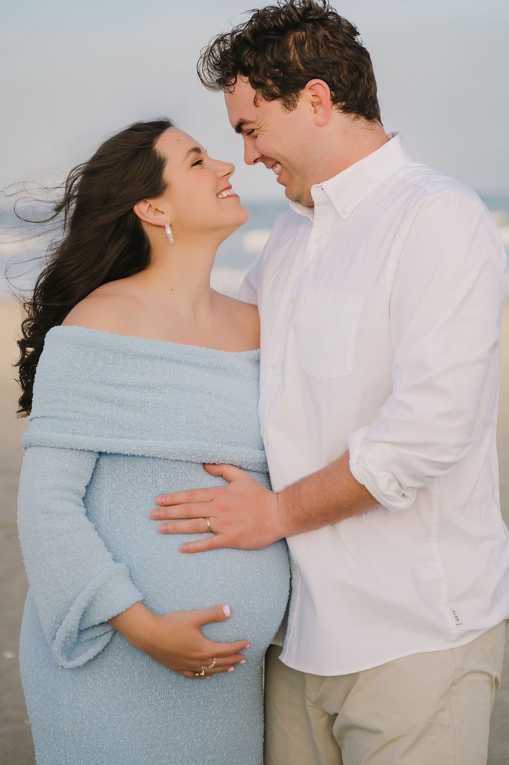 Romantic maternity photo shoot on the beach with couple in light blue dress and white shirt.