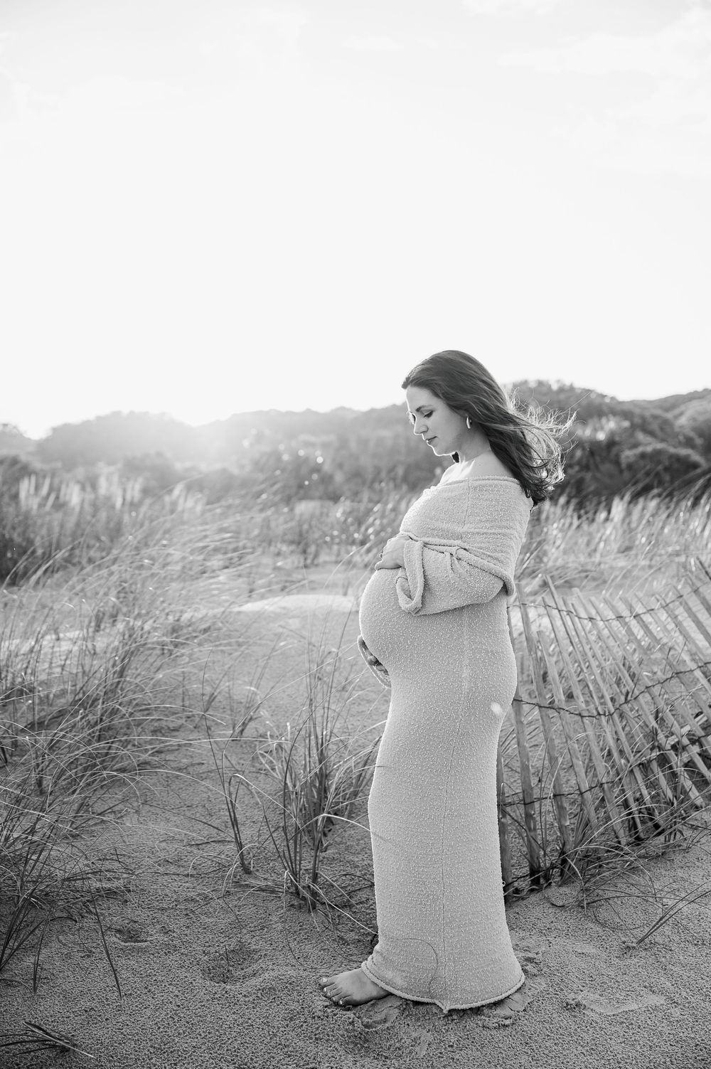 A beachside maternity session with someone wrapped in a cozy knit sweater among sand dunes.