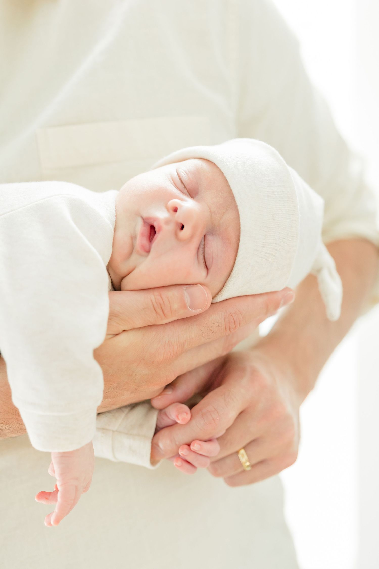 A sleeping newborn baby wrapped in white clothing is gently cradled in caring hands.