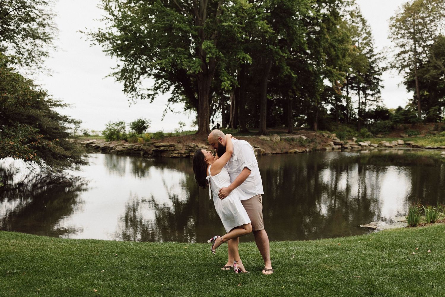 A romantic moment captured by a serene lake surrounded by lush greenery.