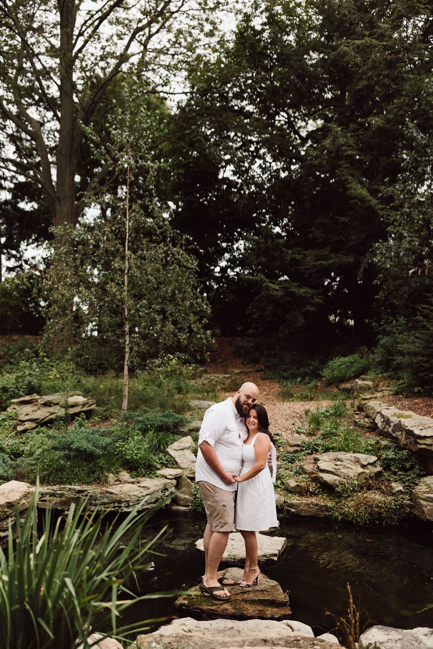 Two people share an intimate moment on stone steps beside a tranquil pond.