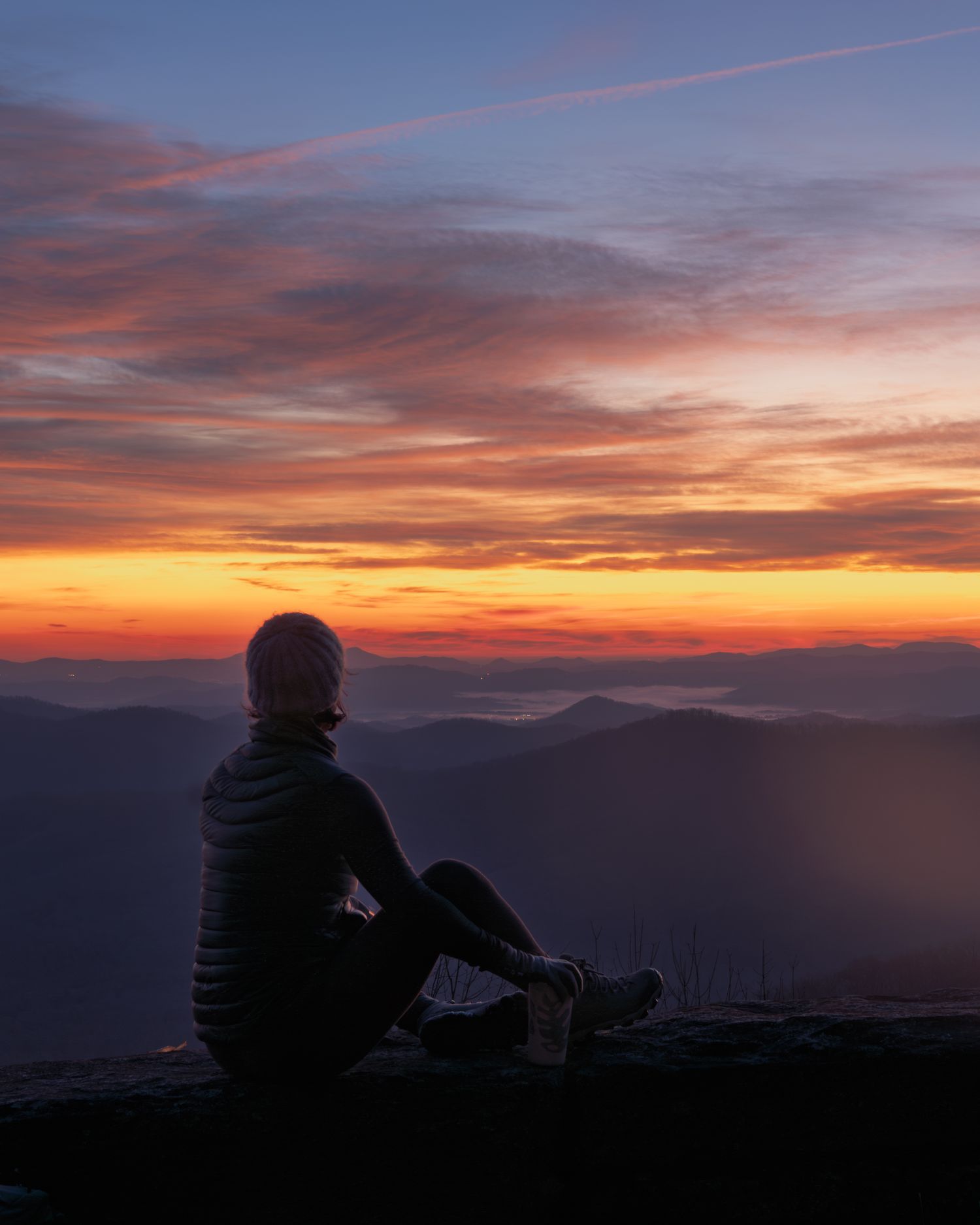 Brand photography image featuring a woman with an insulted mug sitting on a stone wall watching sunrise along the Blue Ridge Parkway