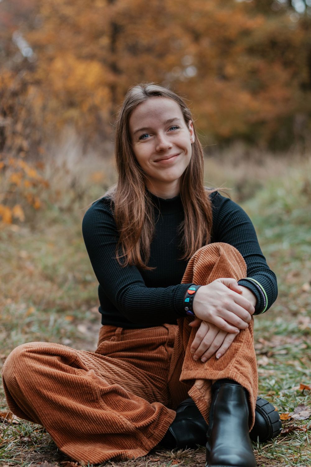 Person in casual outfit sits on grass during fall season.