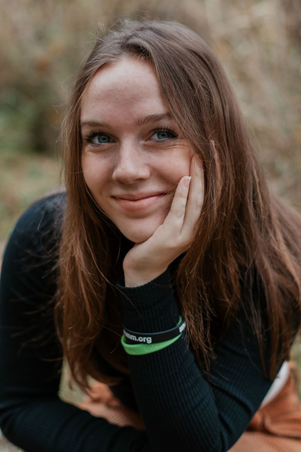 Person in black sweater with green accent smiles in close-up portrait.