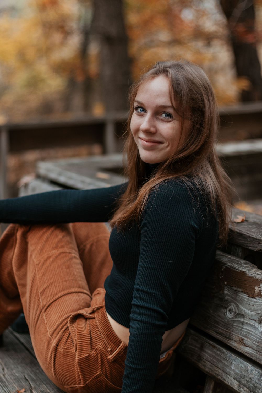 Candid outdoor photoshoot on a wooden bench with autumn colors in the background.