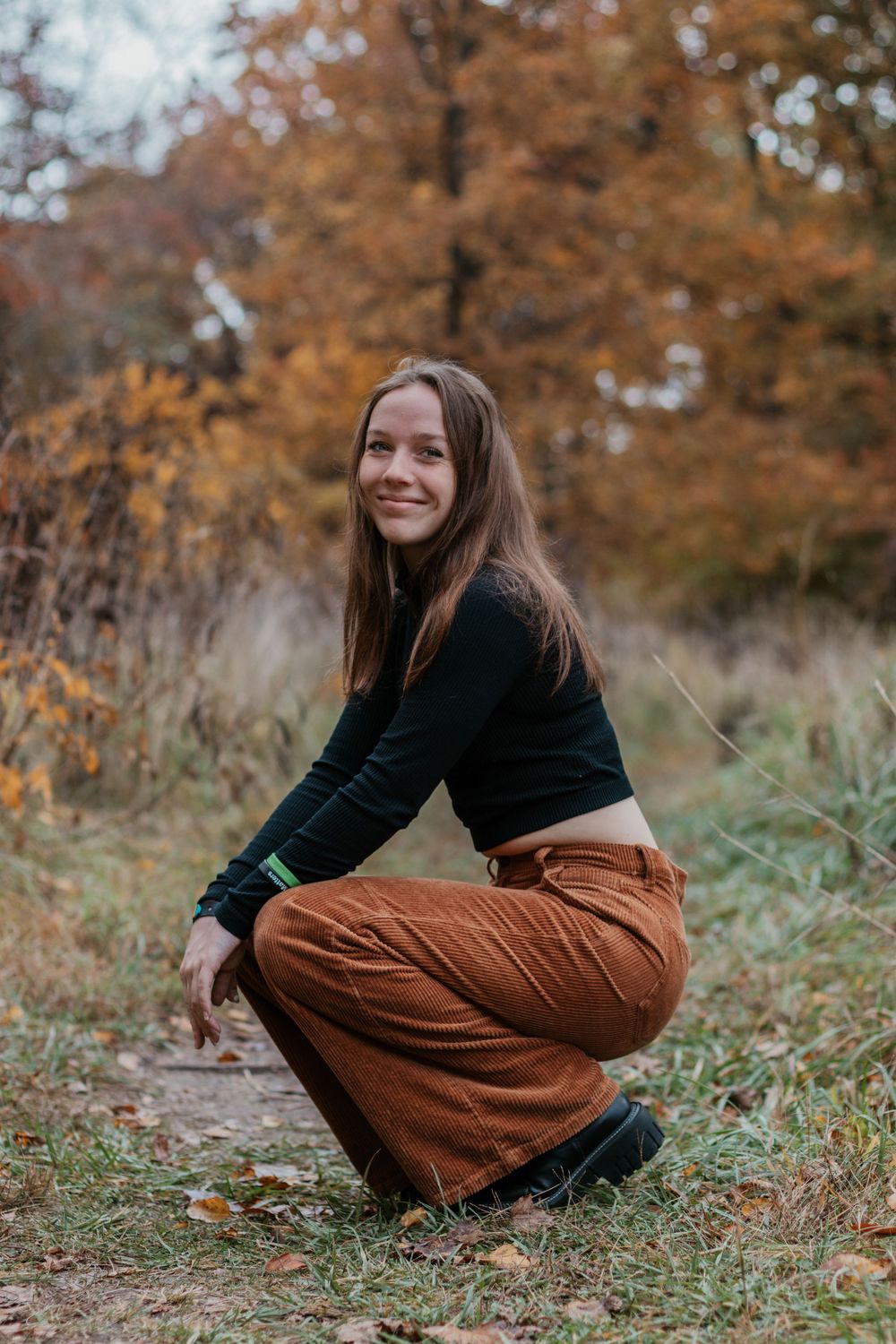 Person in black top and brown pants sits on autumn grass.