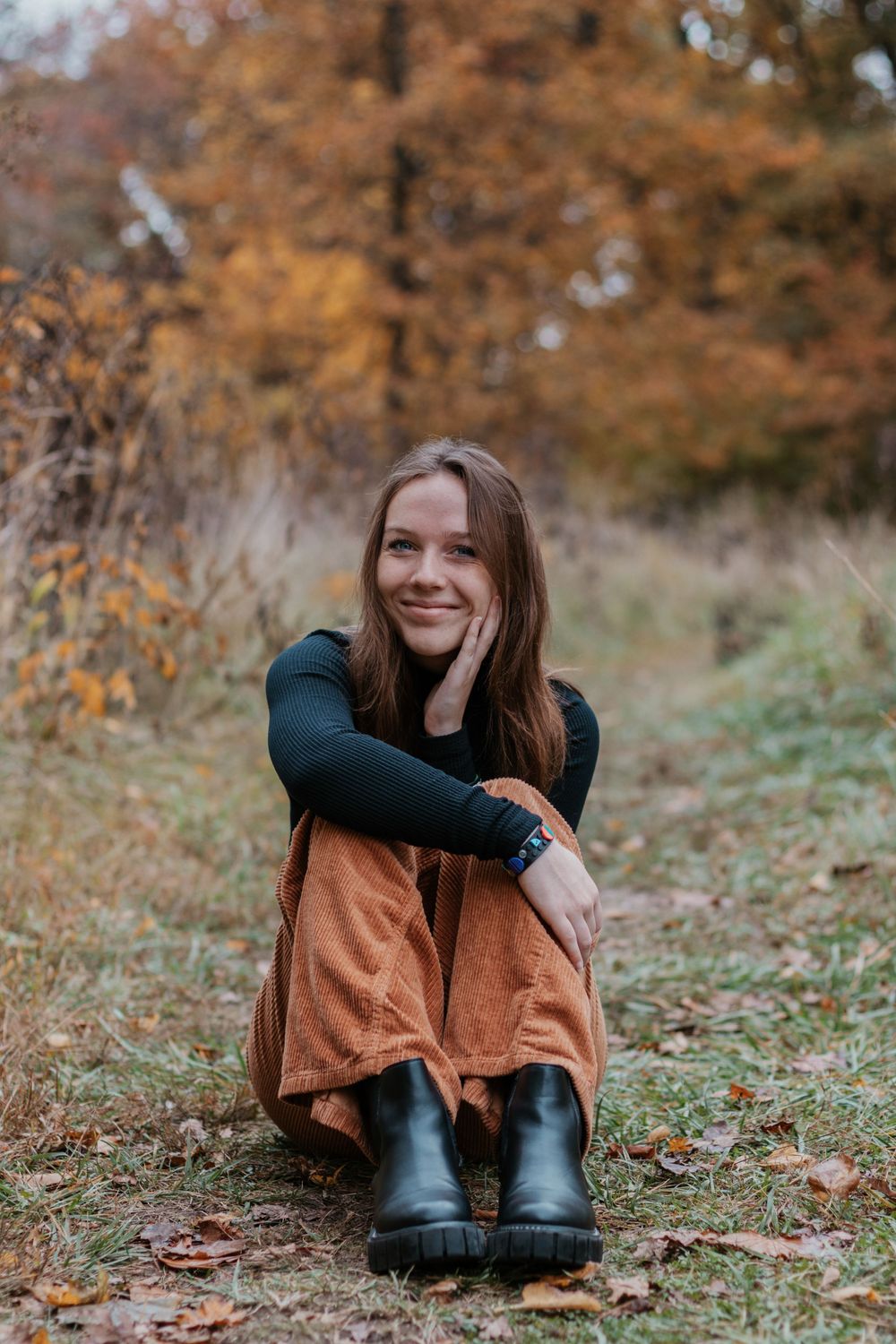 Person in casual attire relaxes on grass with autumn colors in background.