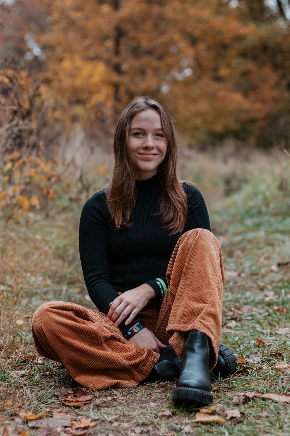 Person wearing black top and corduroy pants sits on fallen leaves.