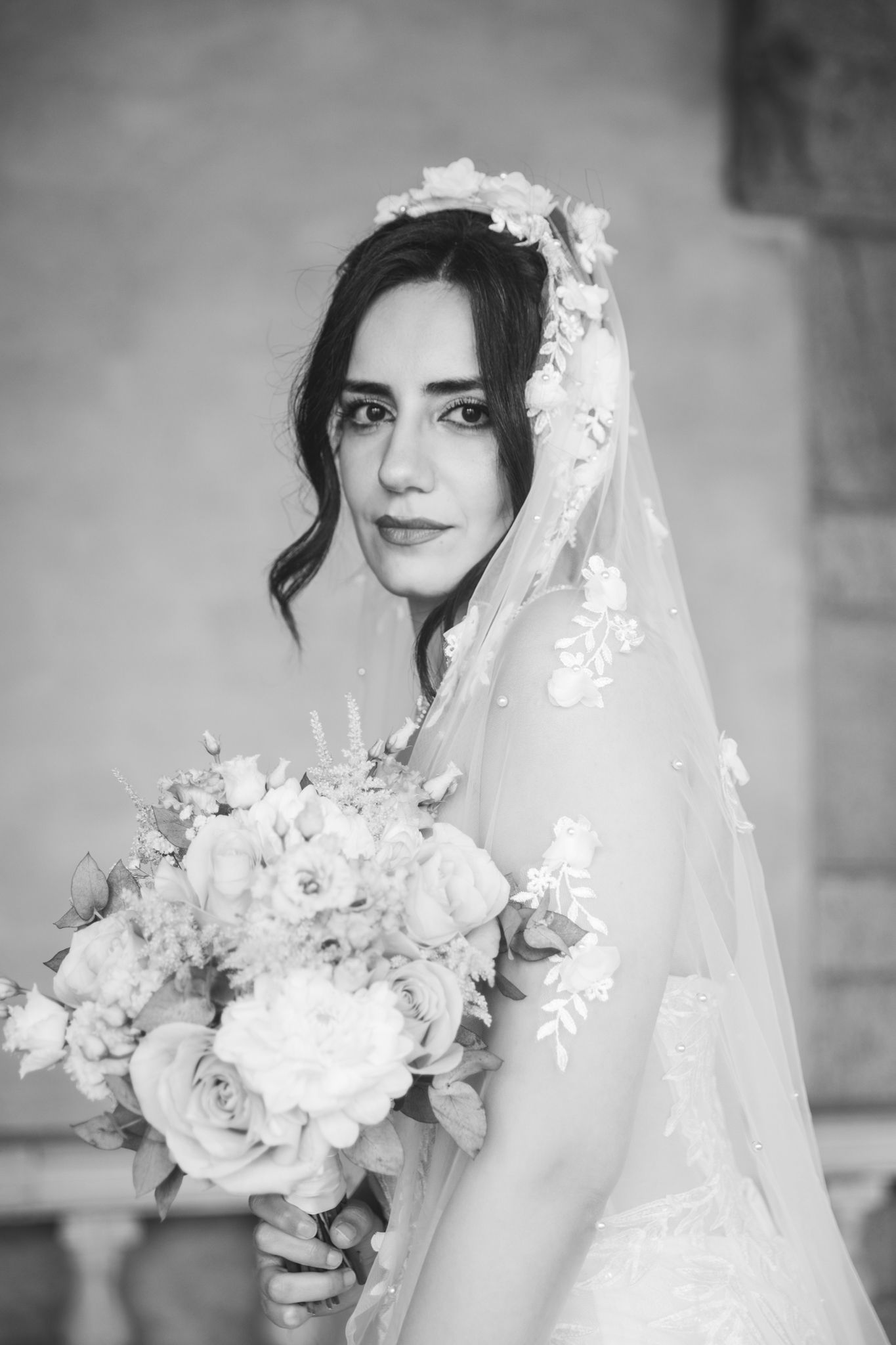 A black and white wedding photo series showing a bride in a veil holding a white floral bouquet.