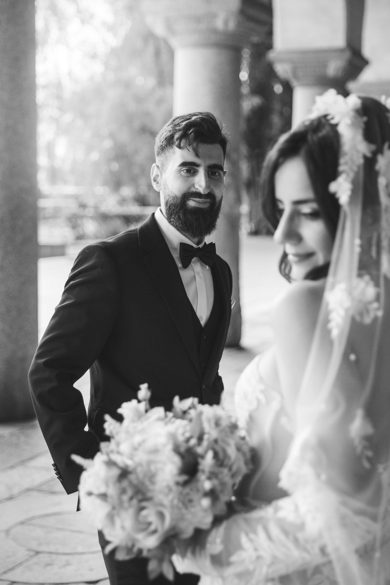 Black and white wedding photos showing tender moments between newlyweds in columned setting.