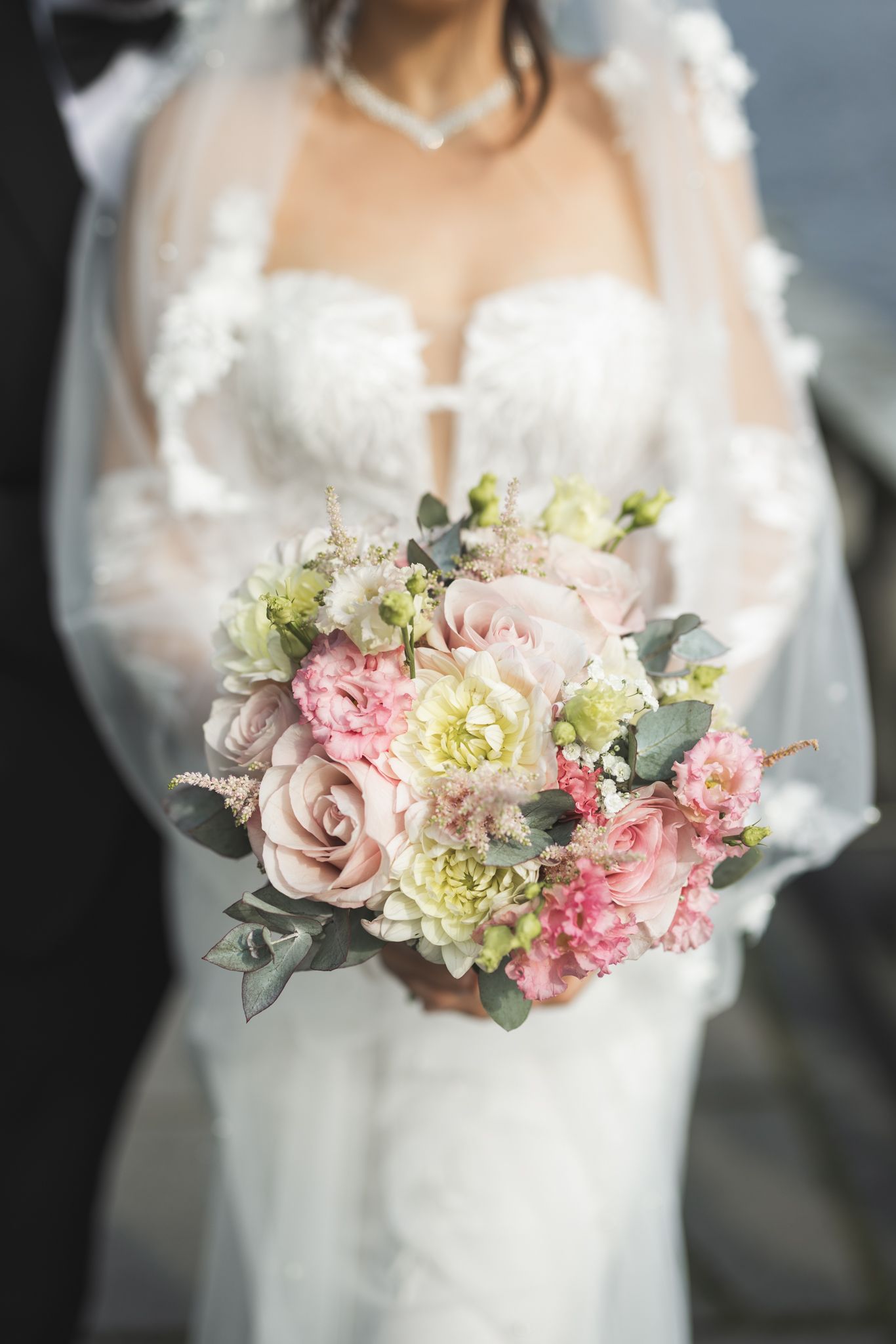 Elegant bridal bouquet featuring soft pink roses, white hydrangeas, and silvery eucalyptus leaves against white dress.
