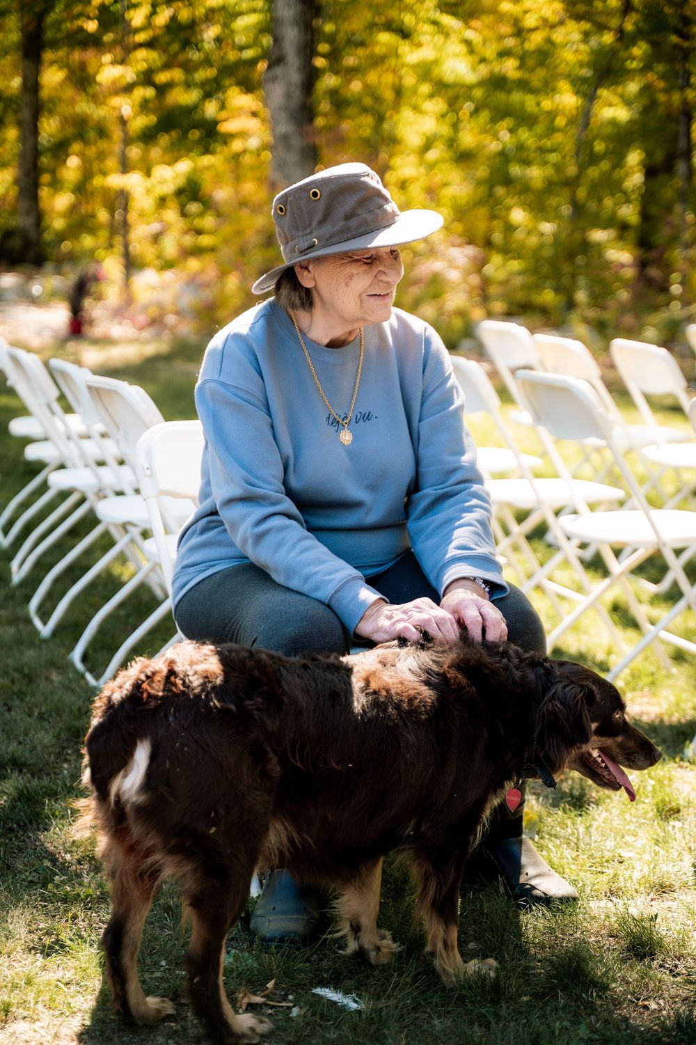 A person in blue sits outdoors on grass with a brown dog on a sunny autumn day.