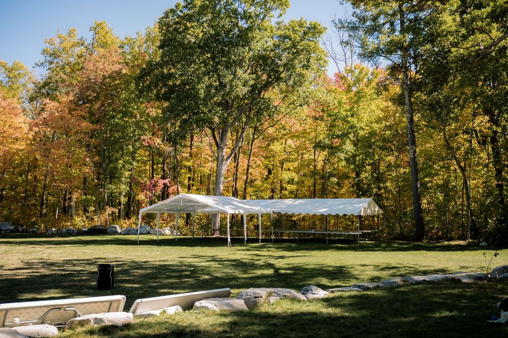 White event tent set up in a clearing surrounded by autumn trees with vibrant yellow and orange foliage.
