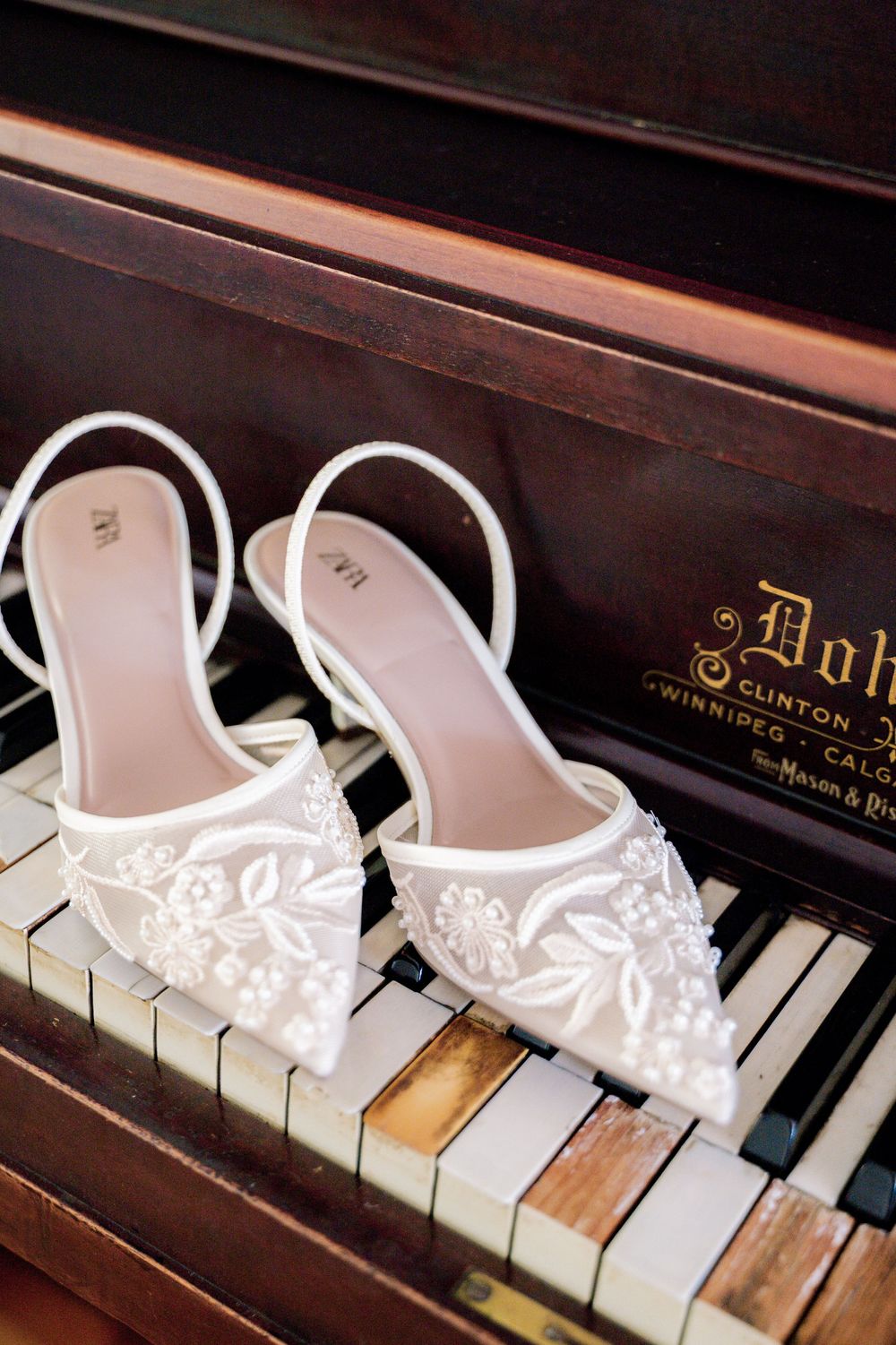 White lace bridal shoes displayed on vintage piano keys.