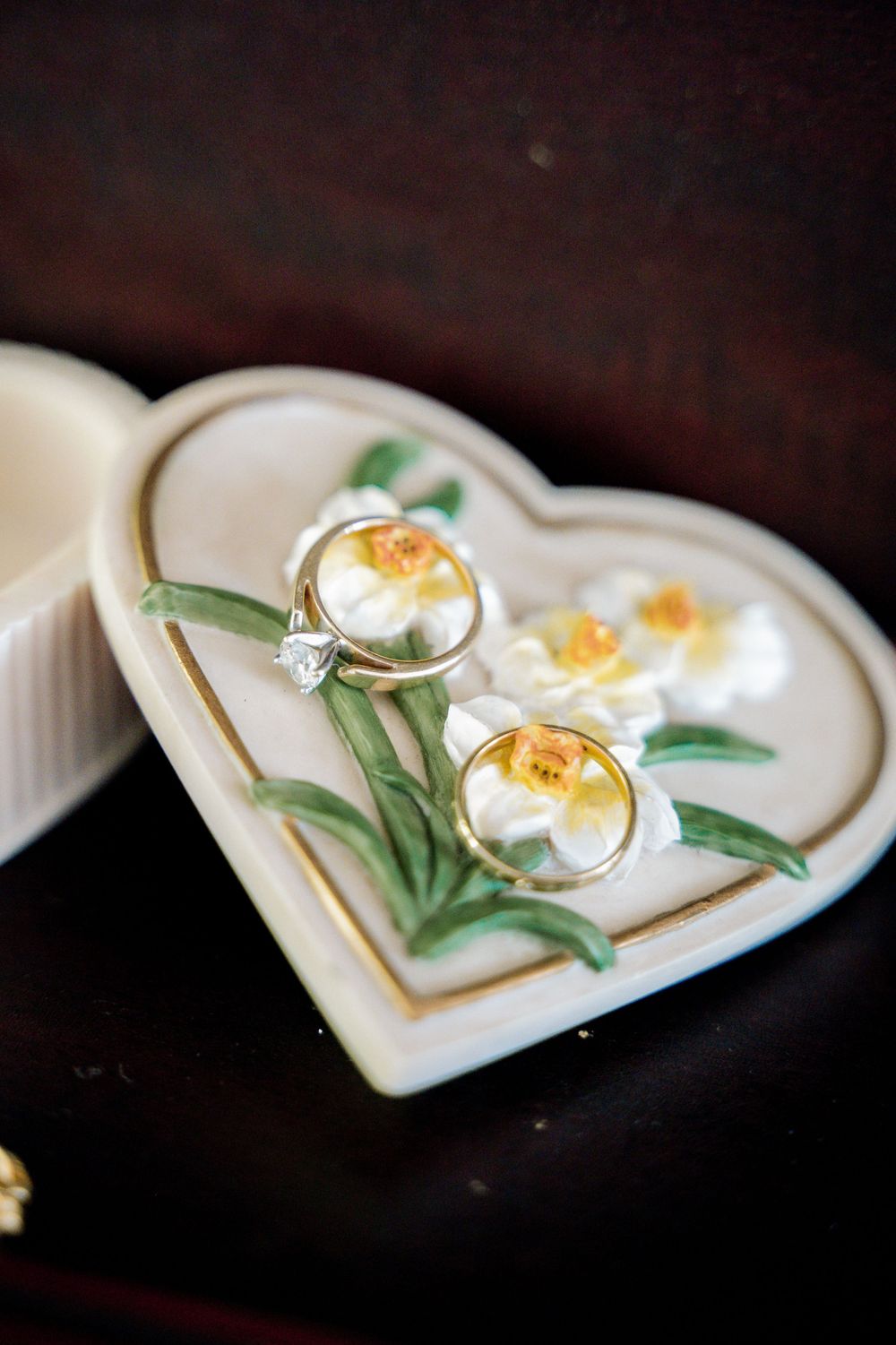 Wedding rings displayed on a decorative heart-shaped ceramic dish with floral design.