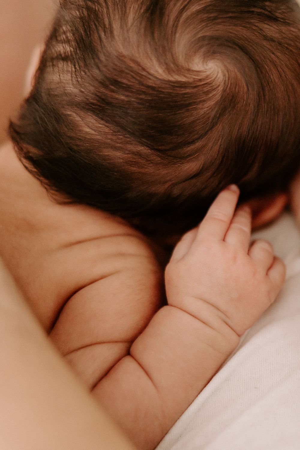 Close-up view of a baby's ear and soft brown hair against a light beige background.