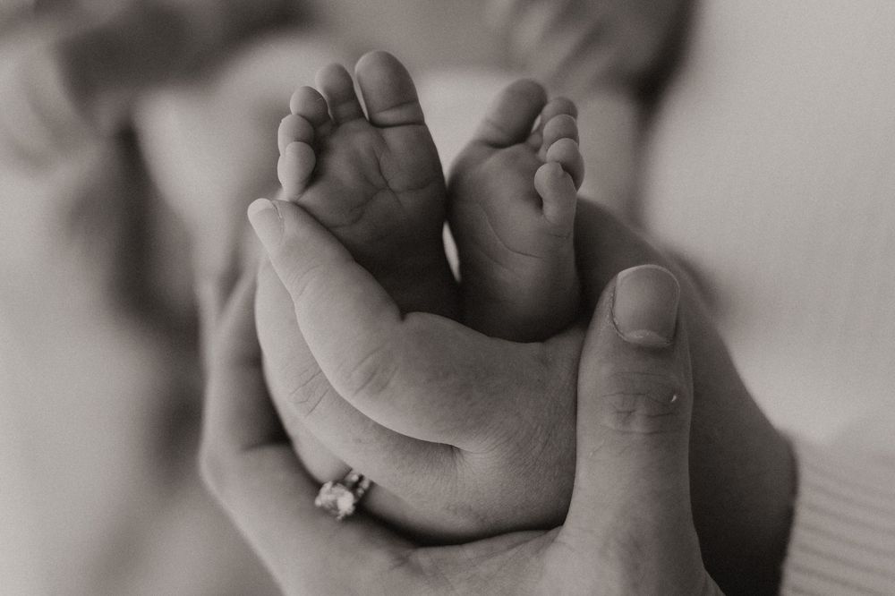 Black and white close-up photo of a baby's tiny feet being gently held by adult hands.