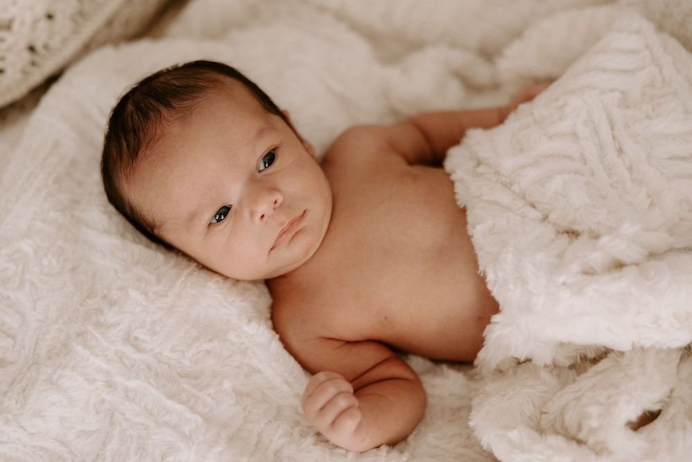 A baby lies peacefully on soft white bedding while being photographed from different angles.