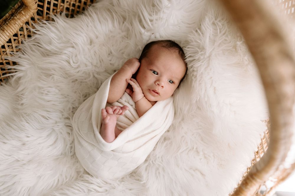 A newborn wrapped in white fabric lies on a cozy fur blanket in a series of peaceful sleeping poses.