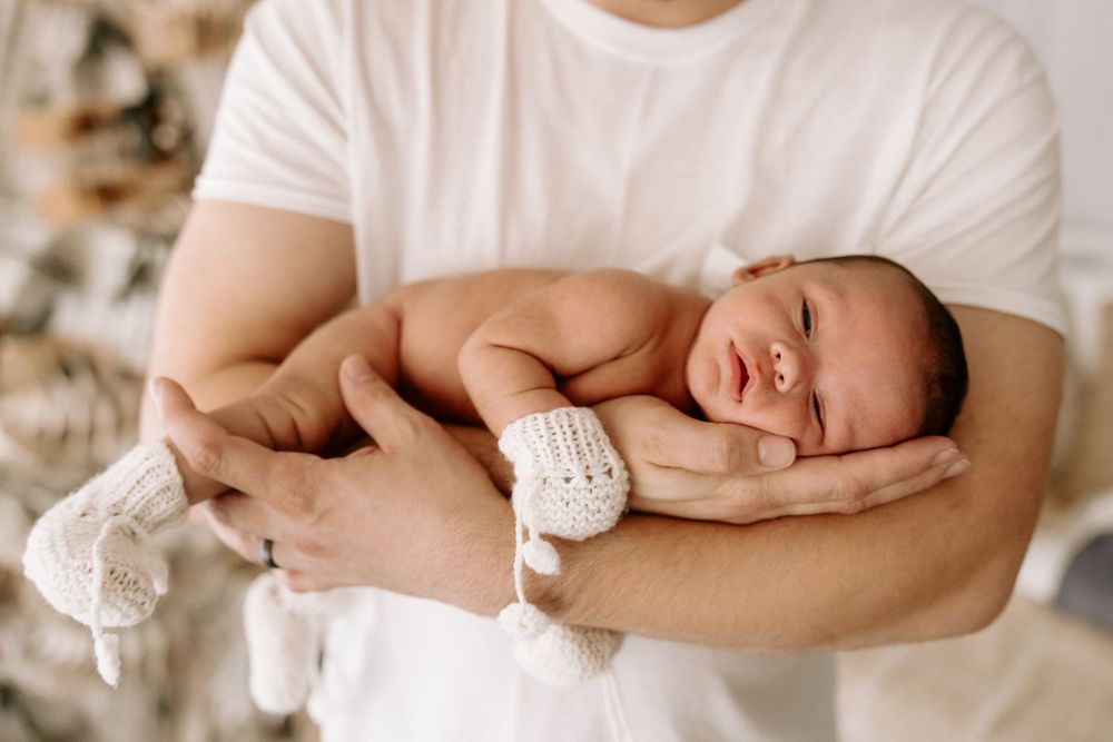 A sleeping newborn baby wrapped in white fabric is cradled gently in someone's arms.