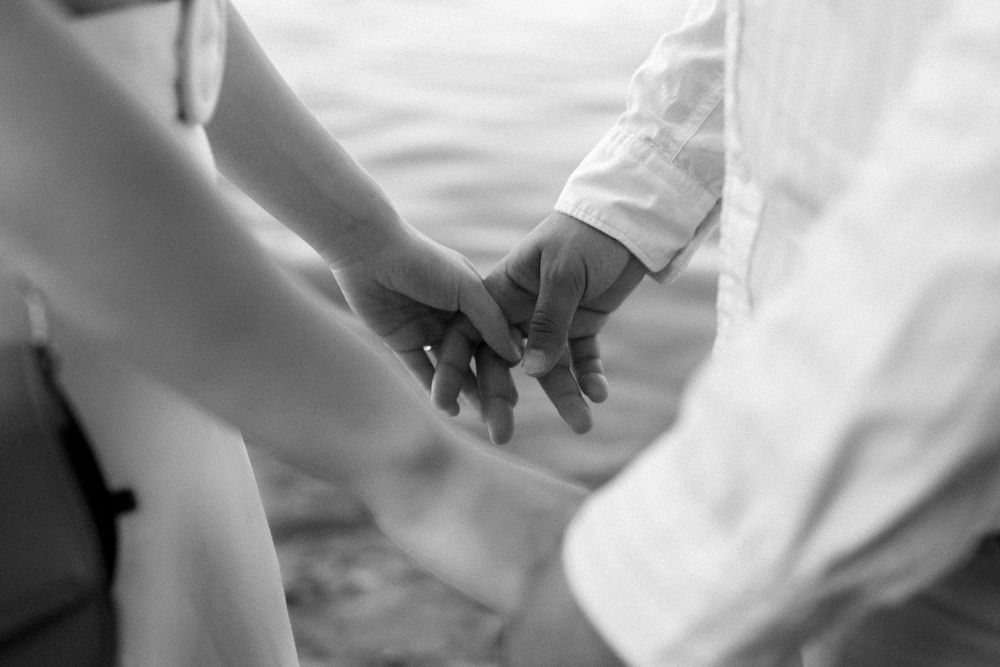 Black and white close-up photograph of two people holding hands tenderly in romantic gesture.