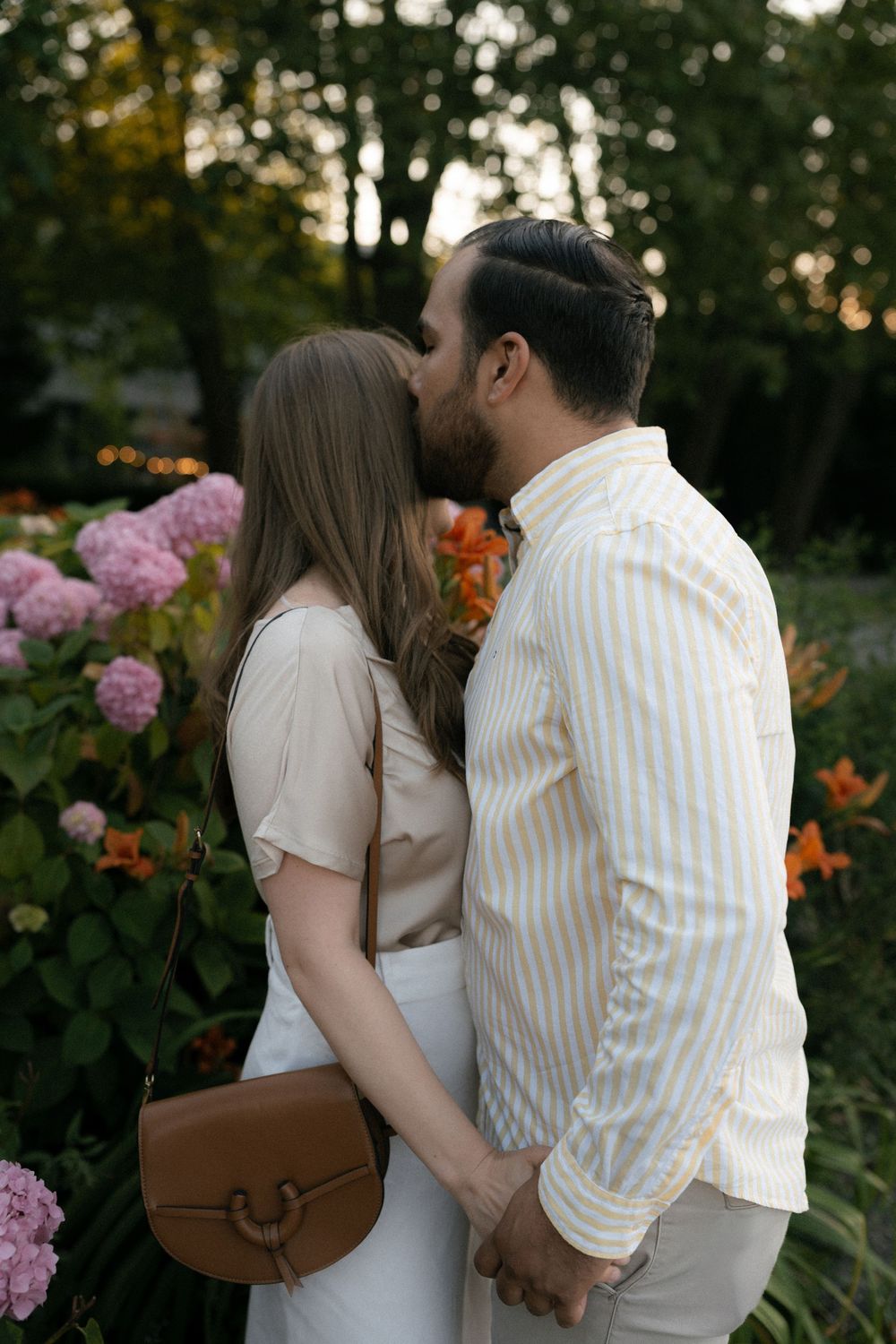 Romantic couple embraces in a garden with pink hydrangeas and orange flowers at sunset.