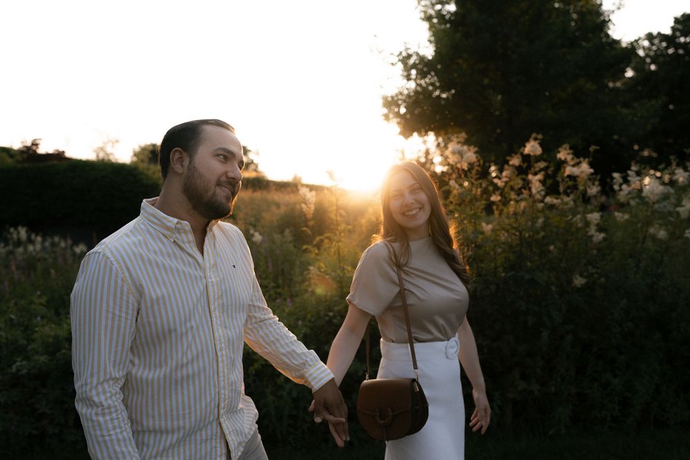 A couple holds hands while walking through a field at sunset with golden light streaming through trees. Luzern