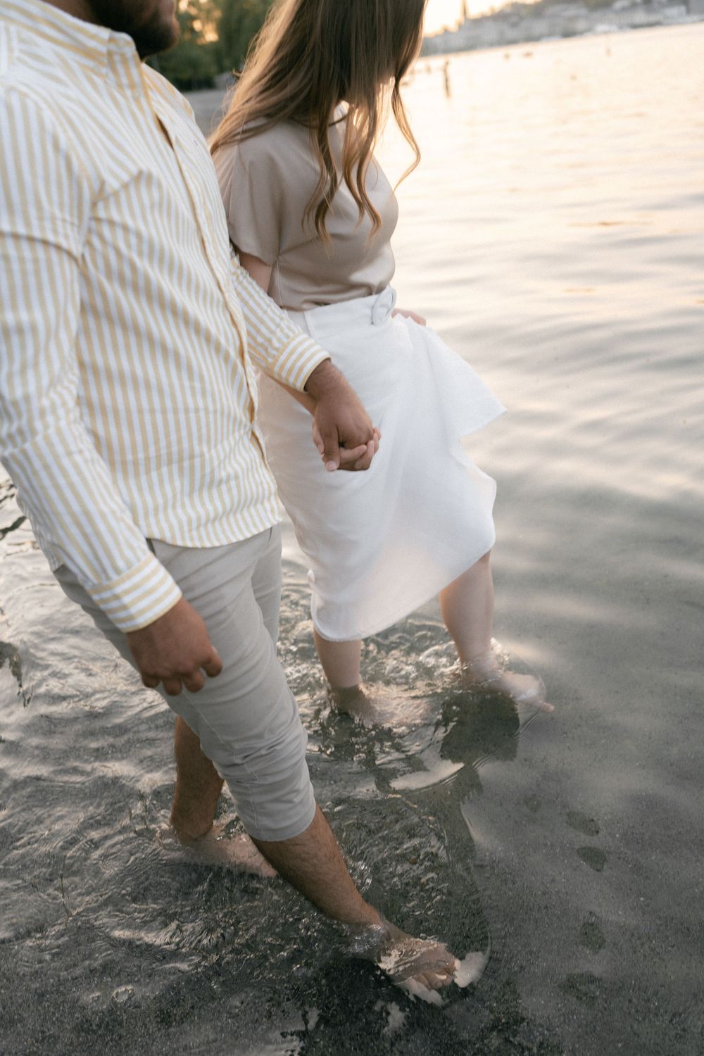 Close-up view of bare feet walking on sandy beach in white linen clothing during sunset.