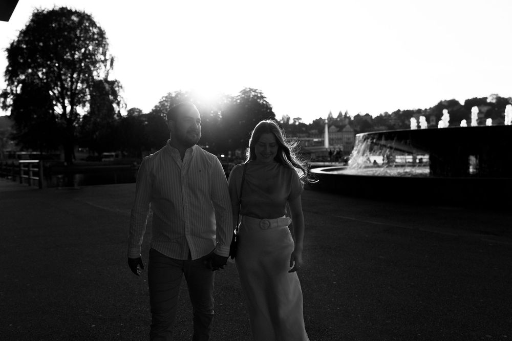 A black and white photo shows two people walking along a path at sunset with trees silhouetted in the background. KKL Luzern