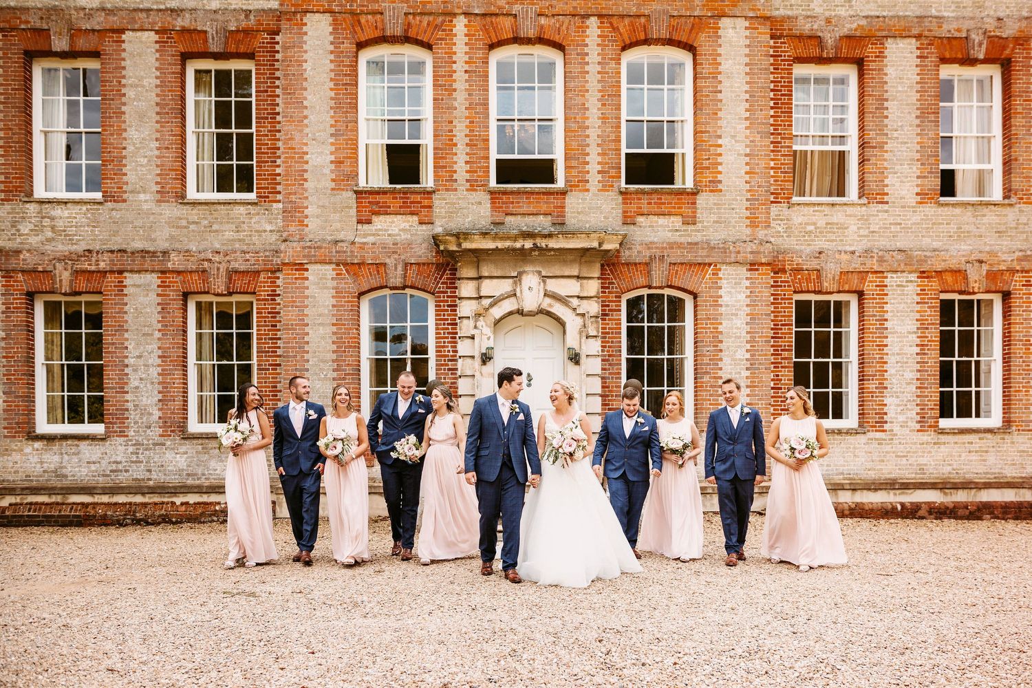 Wedding party stands in front of a grand Georgian brick mansion with symmetrical windows and ornate entrance.