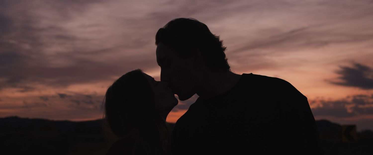Silhouettes of hands reaching towards each other against a dramatic sunset sky.