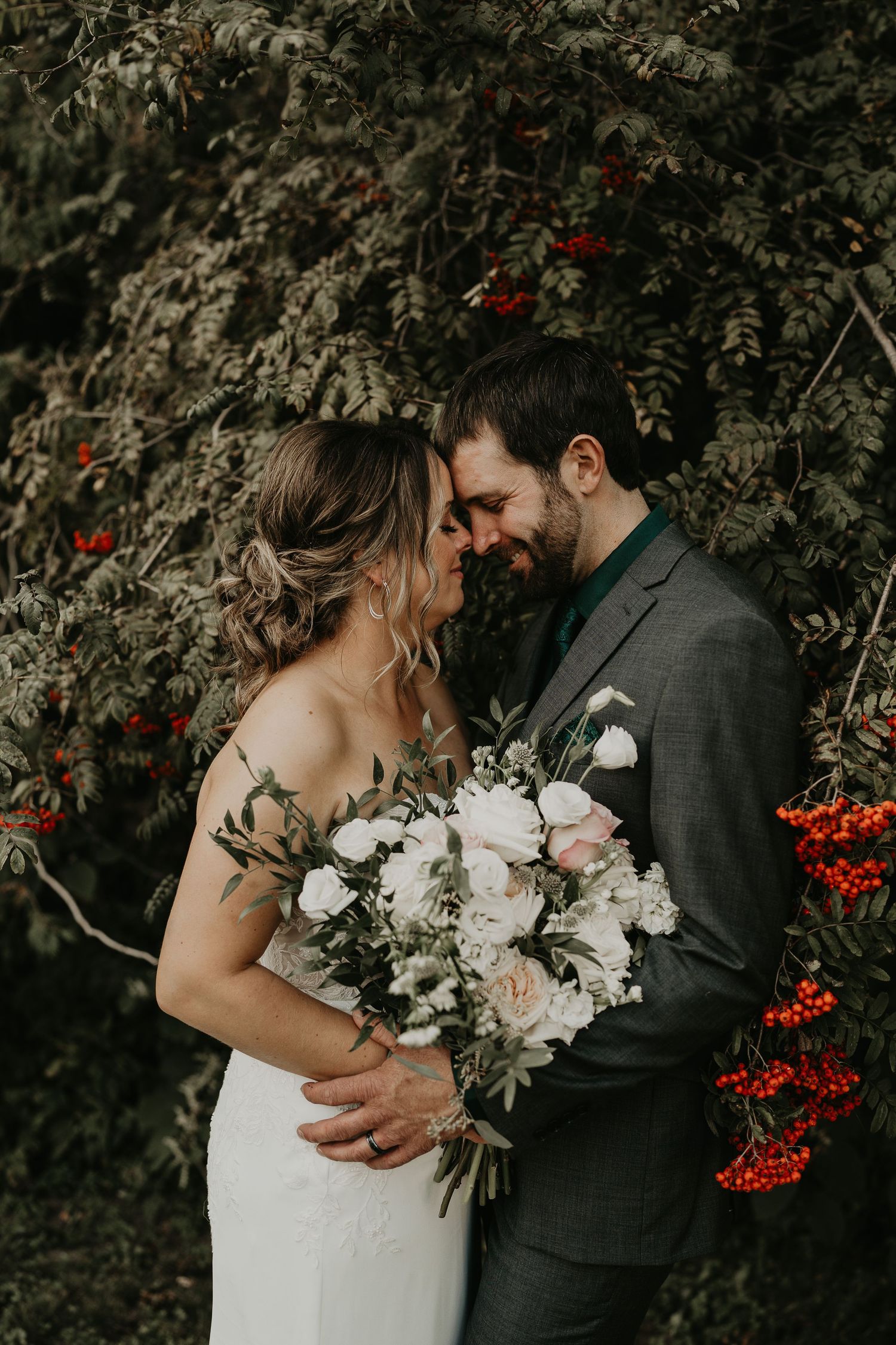 bride and groom face each other under a tree of red berries