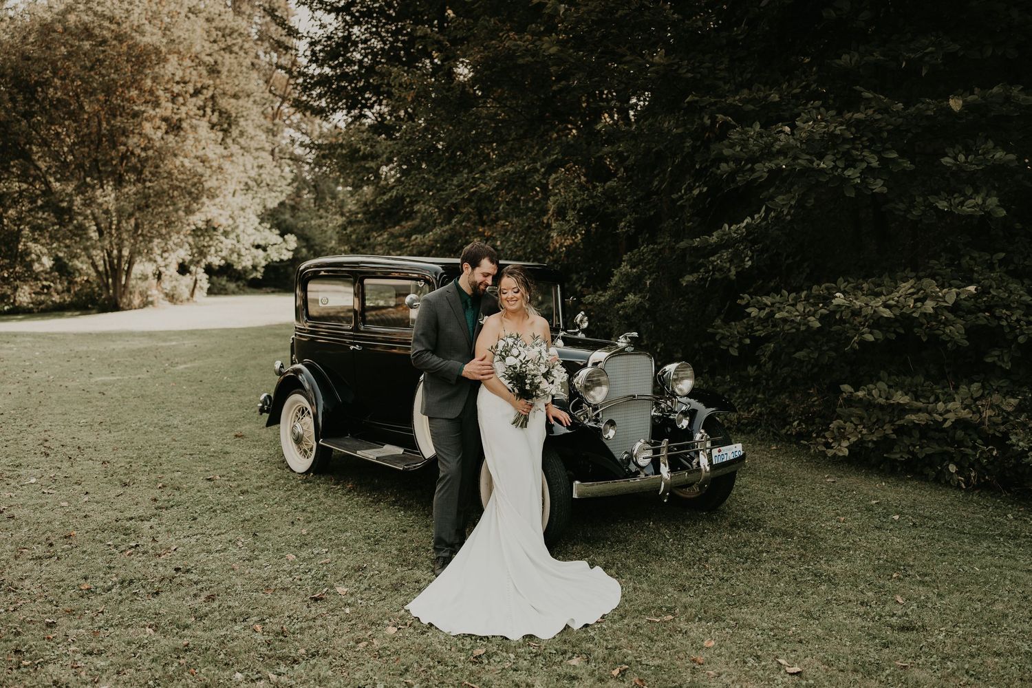 bride and groom in front of a 1930's black sedan with shiny chrome finish and white wall tires