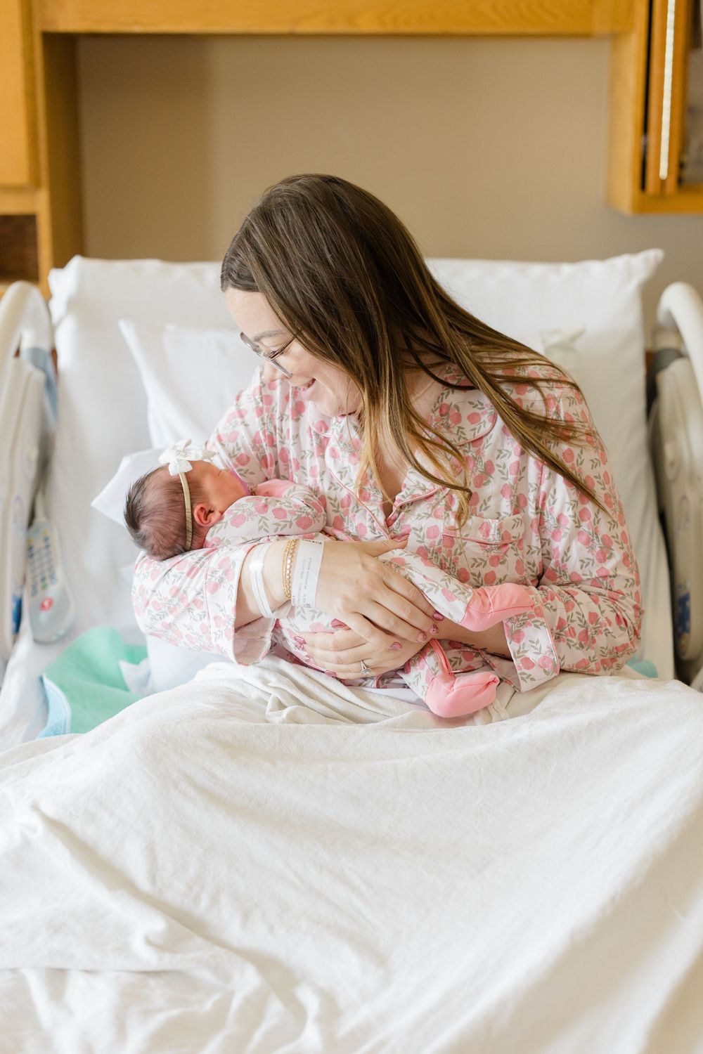 Mother in hospital bed resting with newborn baby during first days after birth.
