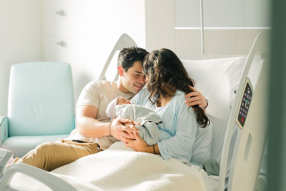 A couple shares an intimate moment in a hospital room while cradling their newborn baby.