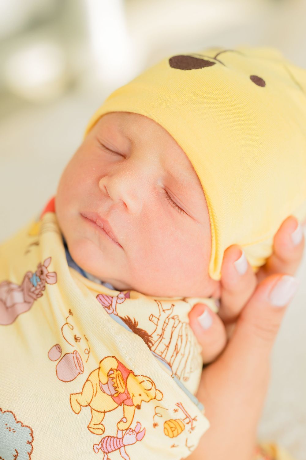A sleeping newborn baby wearing a soft patterned onesie with cartoon animals rests peacefully.