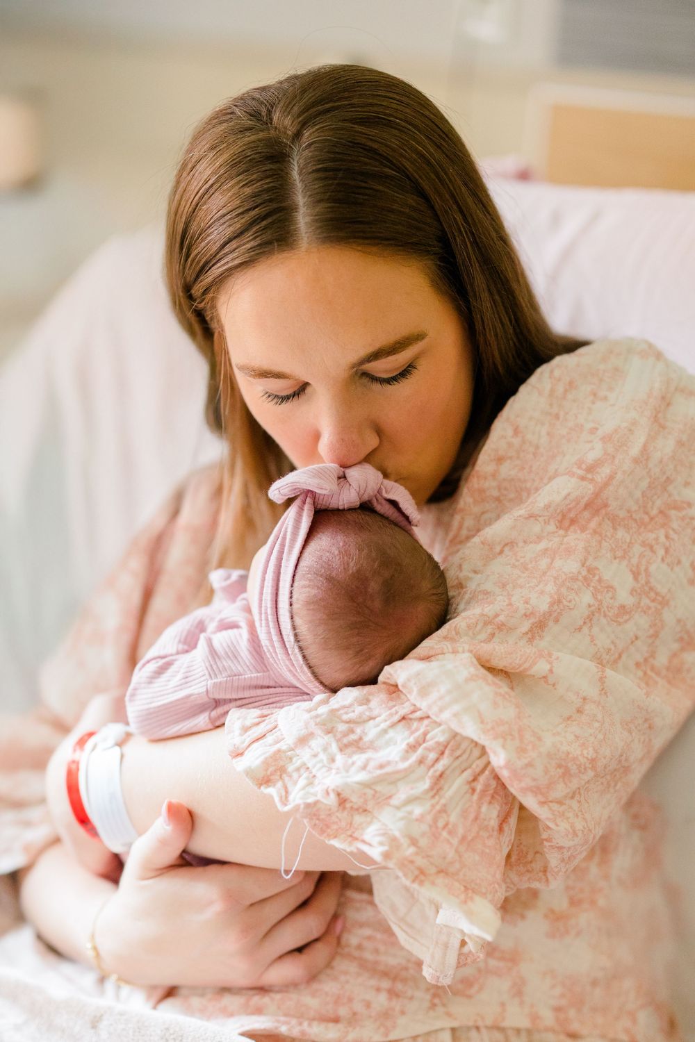 A tender moment between parent and newborn baby in pink clothing, sharing a gentle embrace.