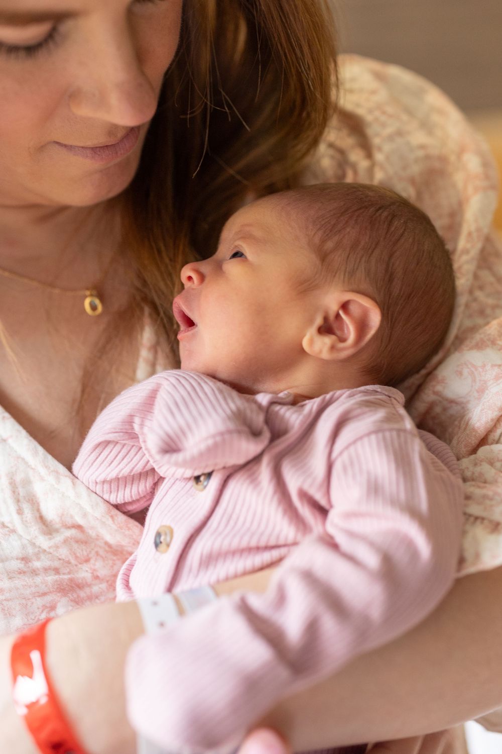 A sleeping baby wearing pink clothing rests peacefully in a caregiver's arms.