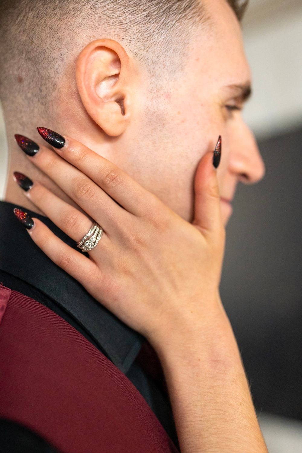 Close-up of bride's hand with diamond ring and black red nail art touching groom's face.
