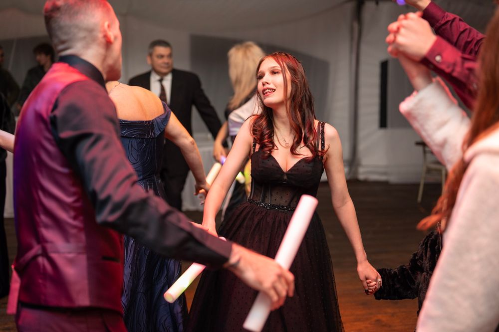 Woman in black evening gown dances holding light stick at elegant wedding reception party.