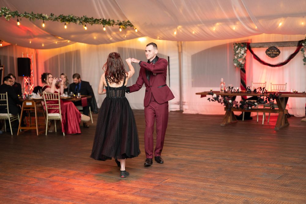 Couple shares a romantic first dance in a warmly lit wedding reception tent with greenery decor.