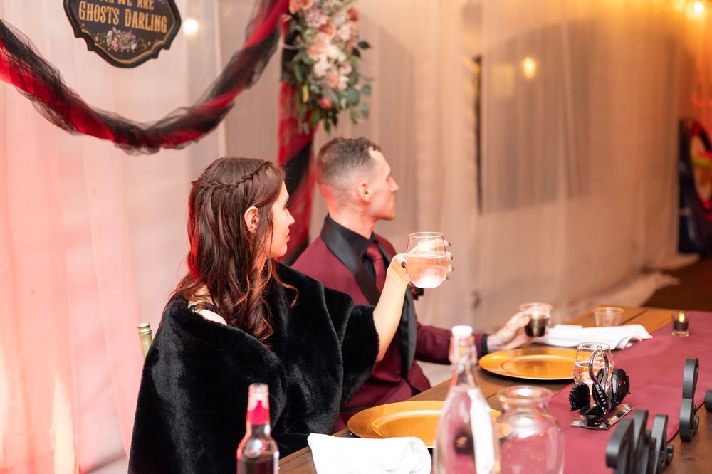 Bride and groom seated at head table during wedding reception with decorative signage in background.