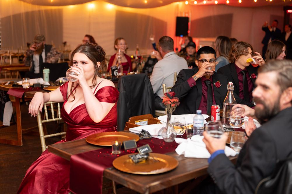 Wedding reception guests in burgundy and black formal attire dining at decorated tables.
