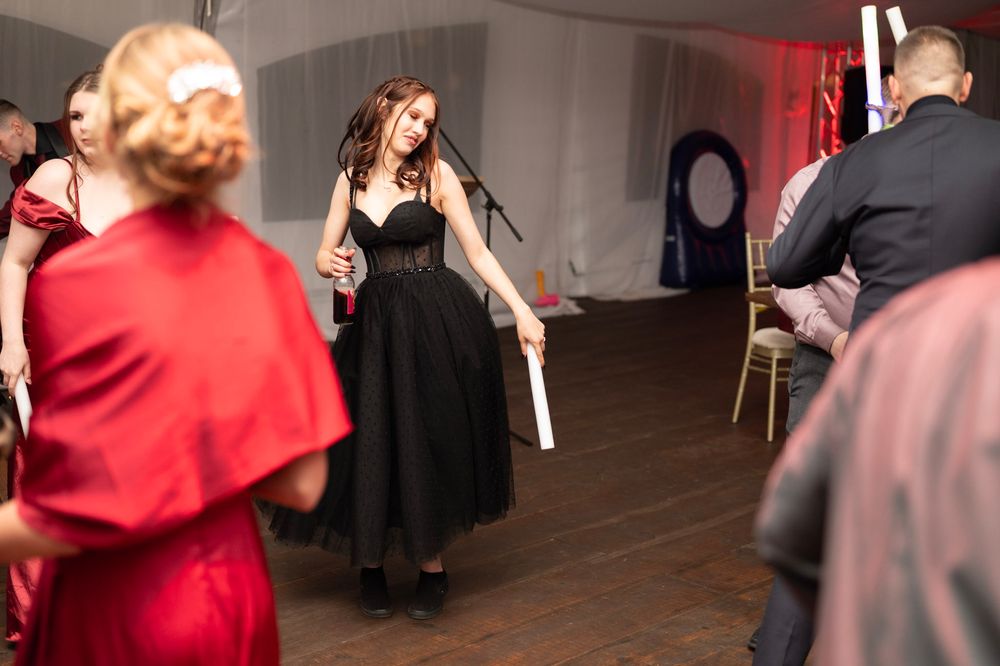 Woman in black dress dancing at wedding reception in white tent with red-dressed guests surrounding her.