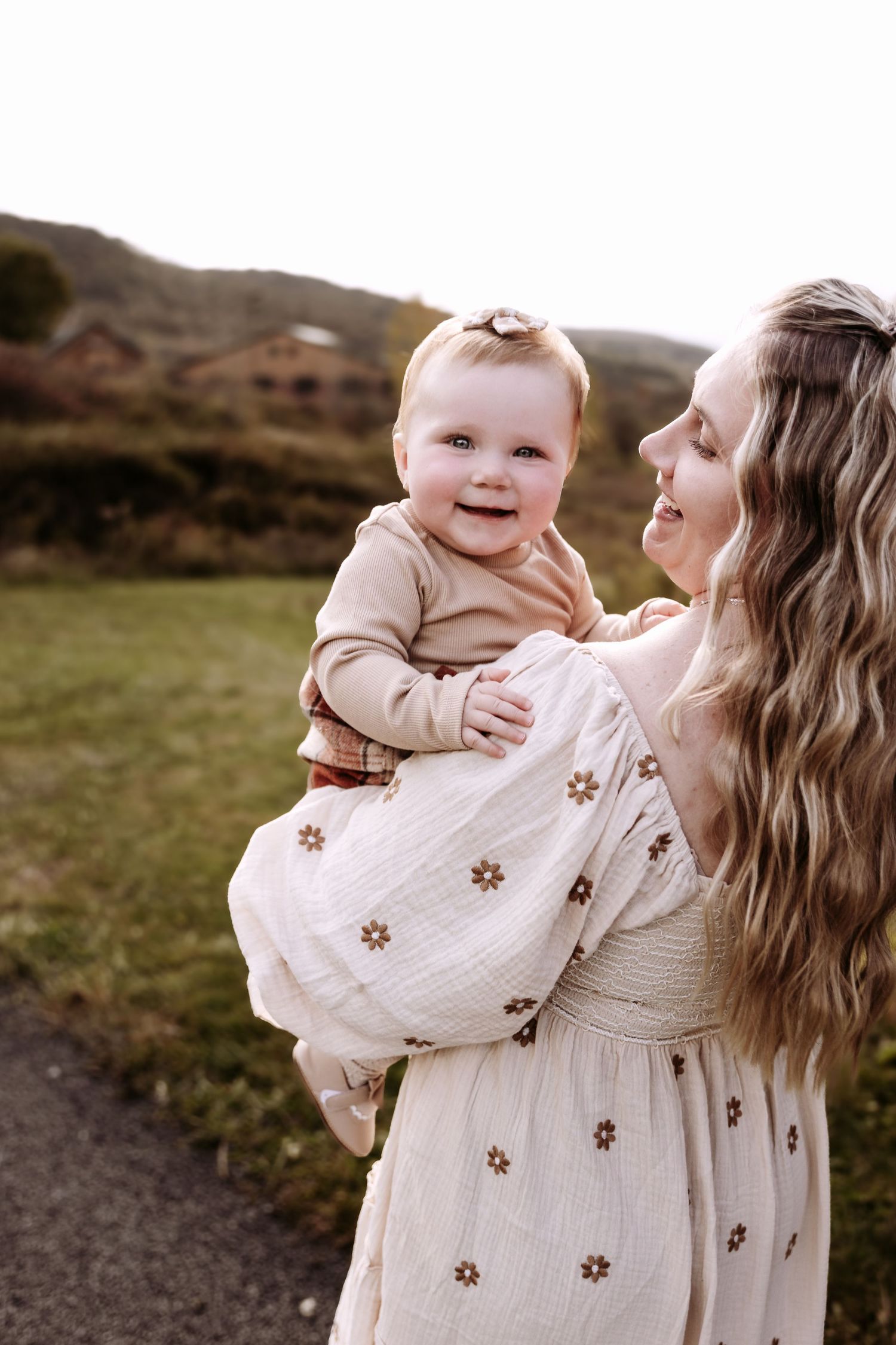 Mother and child wearing matching cream-colored floral dresses share joyful moments outdoors in nature.