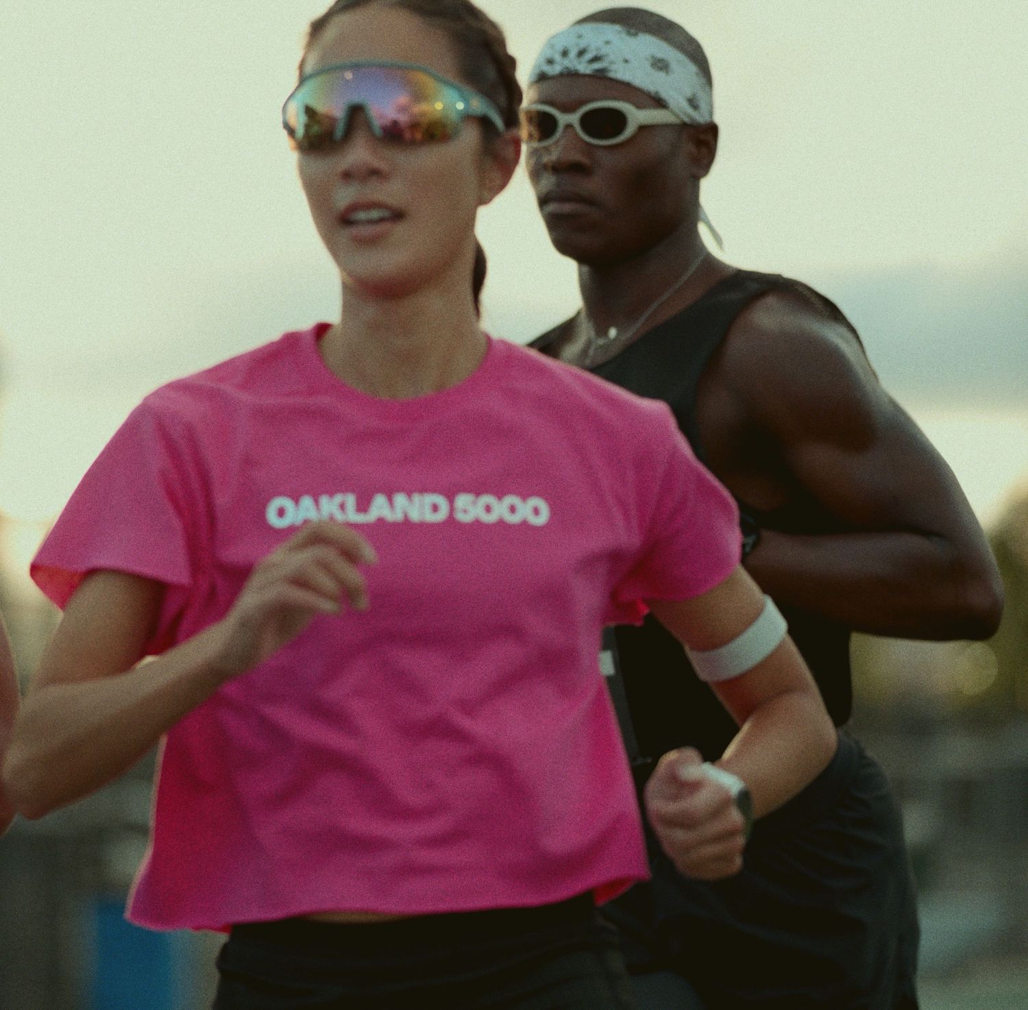 Two runners jogging side by side wearing pink shirts and sunglasses during an outdoor training session.