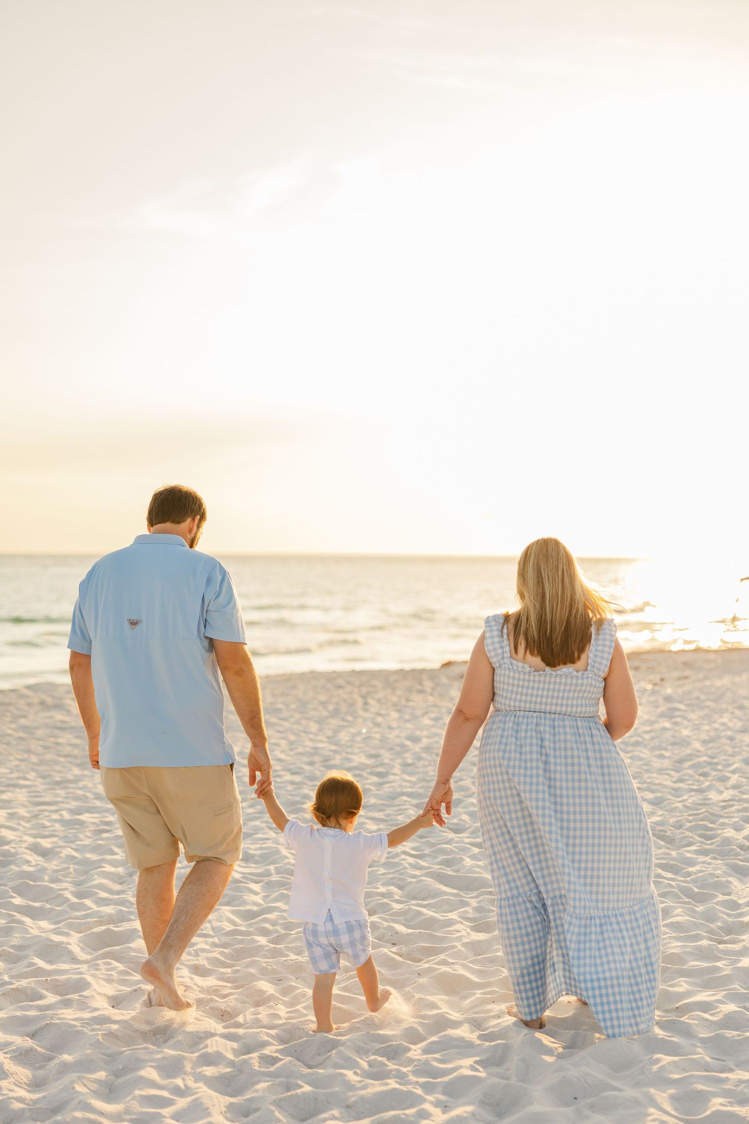 A family enjoys a tender moment together while standing barefoot on a sunny beach at sunset.