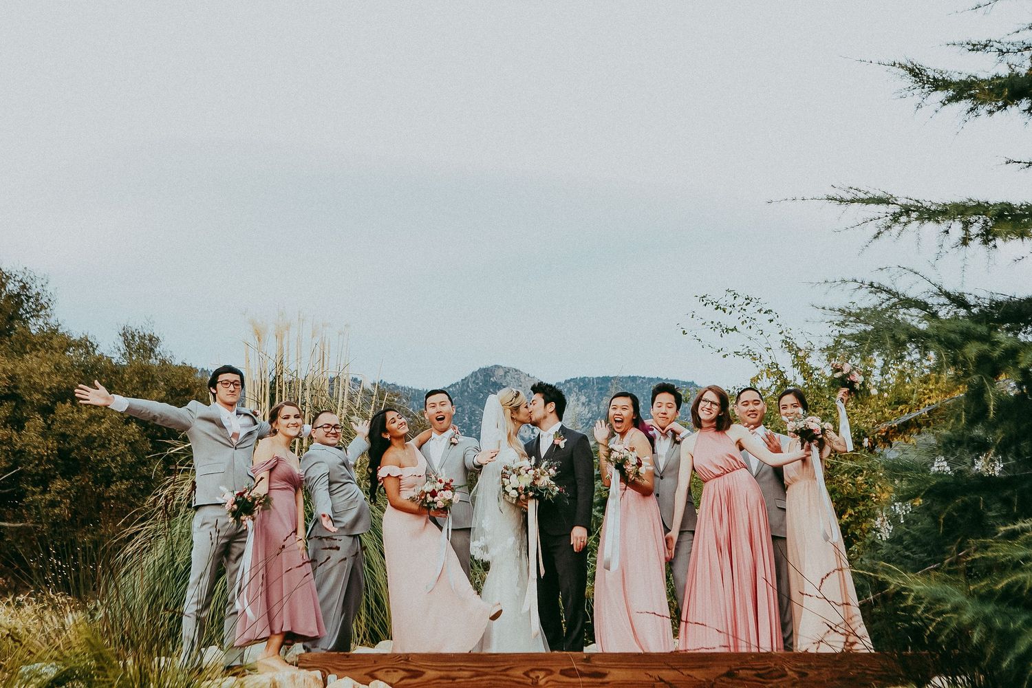Wedding party poses together on a scenic hill overlooking mountains during sunset celebration.