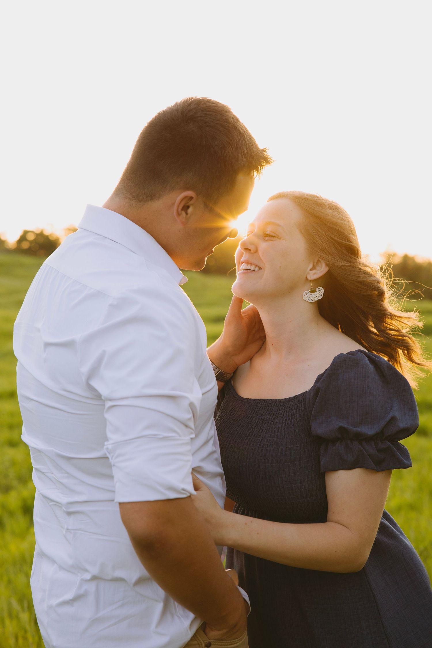 A bride in a flowing white dress stands gracefully on a wooden deck surrounded by evergreen mountains at sunset.