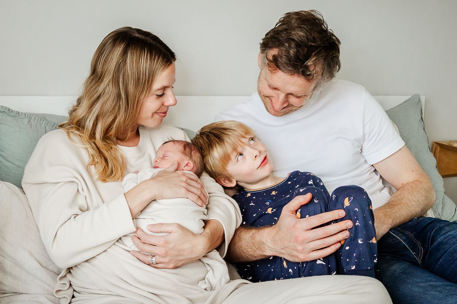 A dad looks relaxed and happy as he sits on the bed at home with his family during a newborn photoshoot with Bristol baby photographer